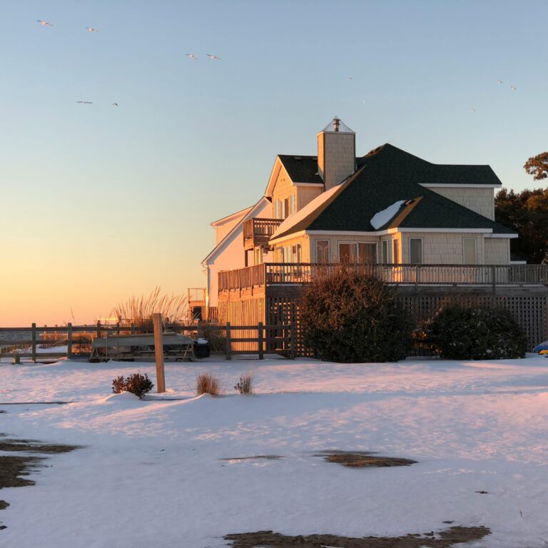 Charming beach house in Kill Devil Hills, NC, covered in snow during a serene sunset.