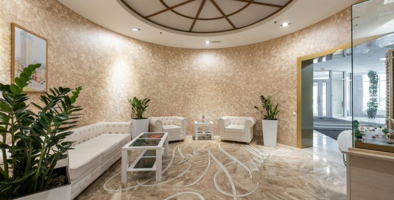 Interior of spacious lobby with comfortable white sofa and armchairs placed in contemporary hotel in daylight